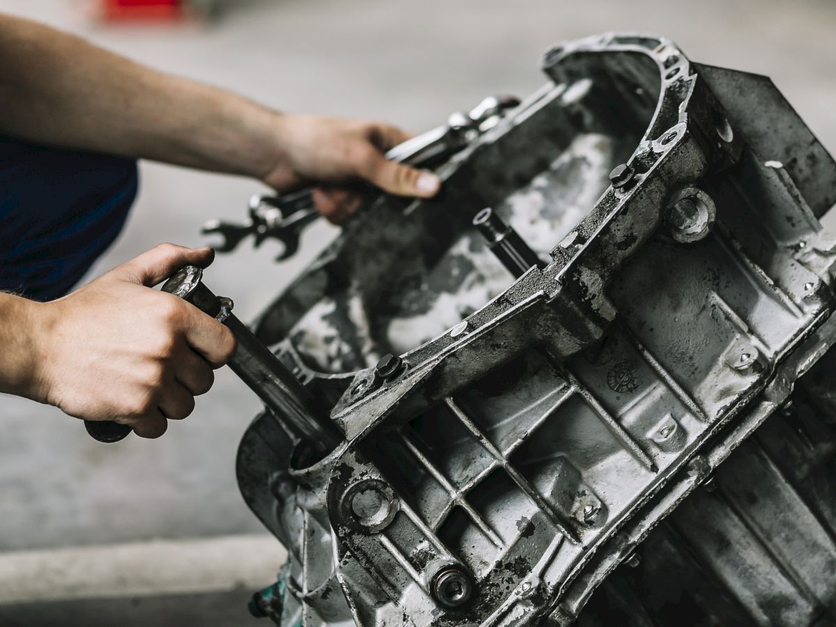 Someone working on a car's gearbox or transmission with tools in a garage or workshop, holding and adjusting the mechanical part.