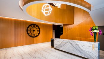 A modern lobby with a curved wooden ceiling, large wall clock, marble reception desk, and flower arrangement.