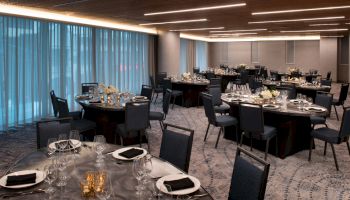 A banquet hall with round tables, each set with elegant tableware and black napkins, surrounded by chairs, and soft lighting draping the room.
