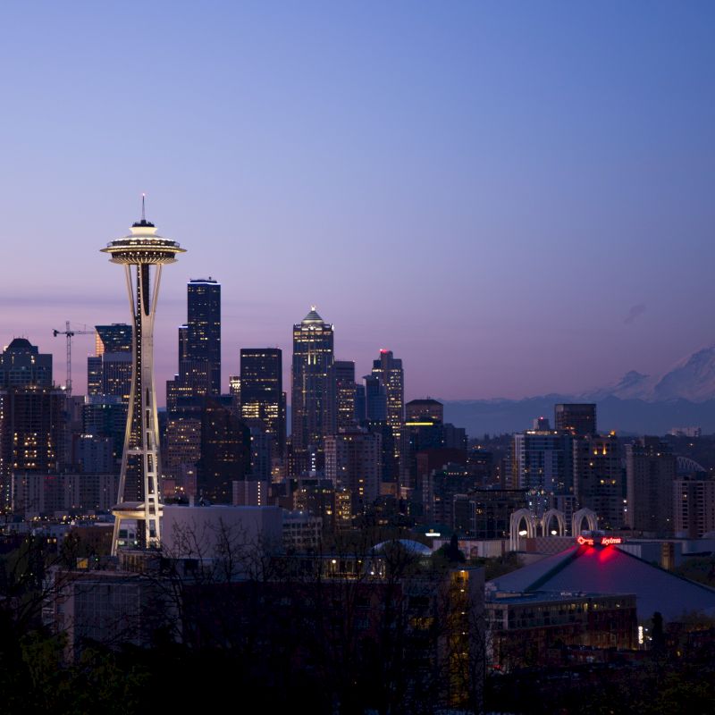 The image shows the Seattle skyline at dusk, featuring the Space Needle prominently, with Mt. Rainier visible in the background.