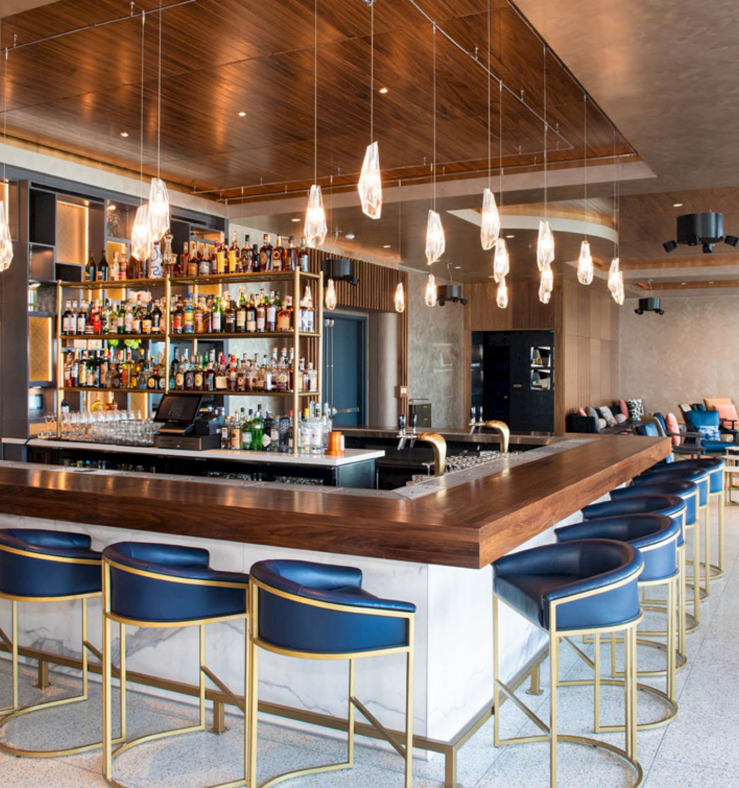 An upscale bar with a modern design, featuring a well-stocked bar area, stylish barstools, hanging lights, and a comfortable seating area in the background.
