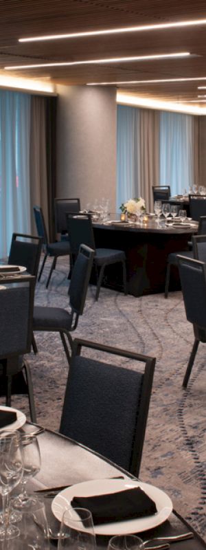 A banquet hall set up with round tables, chairs, and table settings. The room is well-lit with modern lighting and has blue curtains in the background.