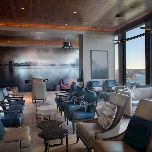 The image shows a sophisticated lounge area with modern seating, large windows offering a scenic view of a Ferris wheel and waterfront.
