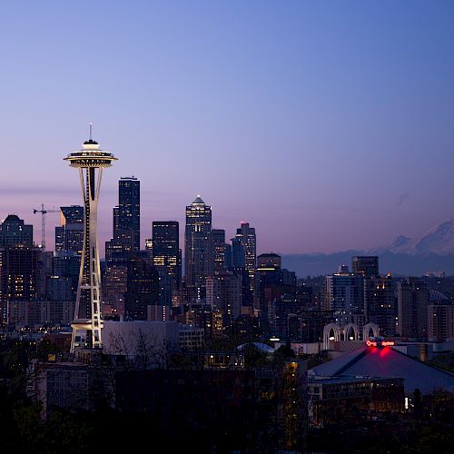 A view of Seattle’s skyline at dusk with the iconic Space Needle prominently in the foreground and Mount Rainier visible in the background.