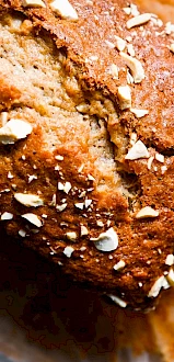 A freshly baked loaf of bread, sprinkled with chopped nuts, sits on parchment paper.